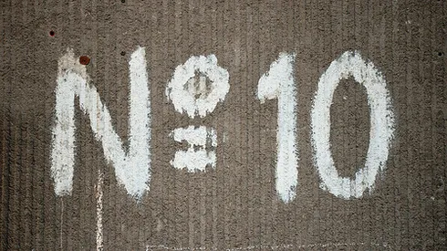 Large number sign with a capital N and the number 10 painted in white on an old building wall with a distinctive texture.
