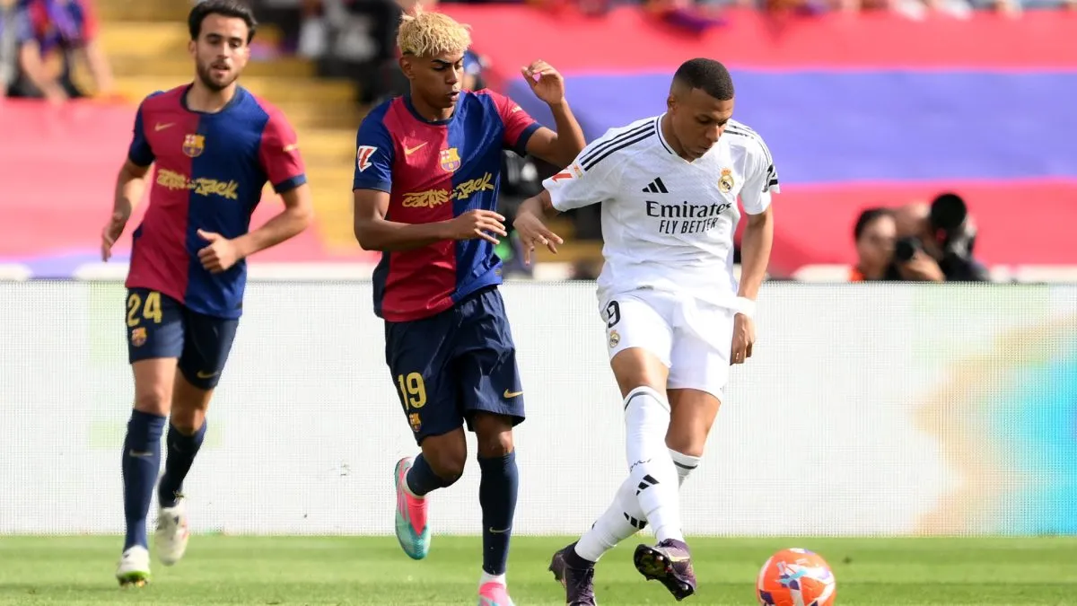Kylian Mbappe of Real Madrid passes the ball under pressure from Lamine Yamal of FC Barcelona.