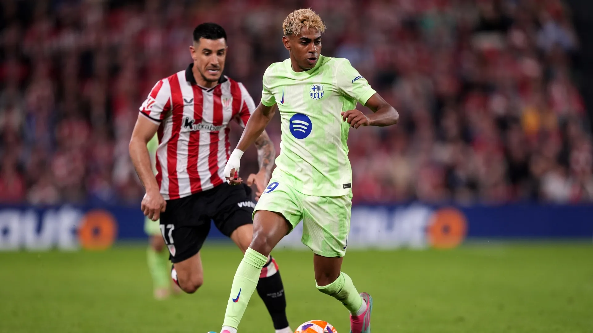 Lamine Yamal of FC Barcelona runs with the ball whilst under pressure from Yuri Berchiche of Athletic Club.