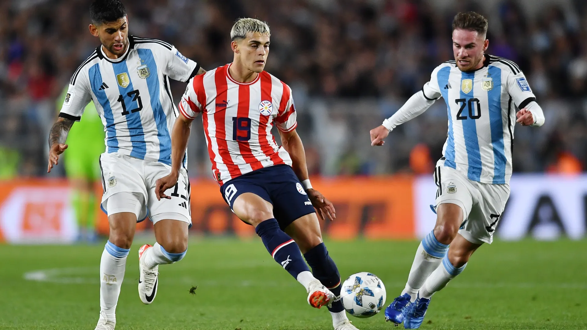 Ramon Sosa of Paraguay kicks the ball against Cristian Romero and Alexis Mac Allister of Argentina.