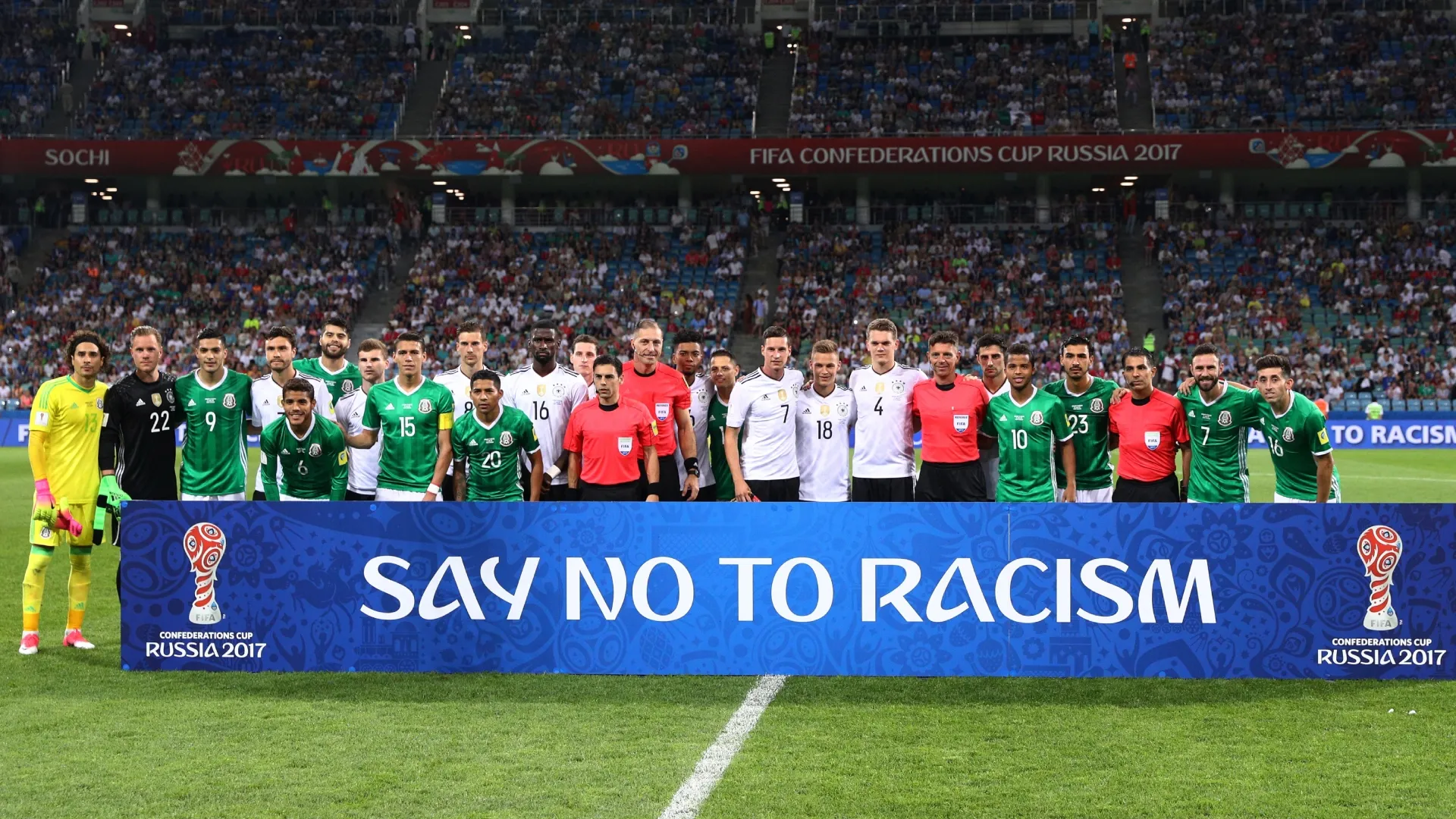 Players and match officials stand with an anti racism banner.
