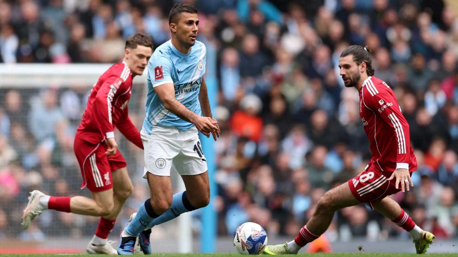 Rodri of Manchester City runs with the ball whilst under pressure from Dominik Szoboszlai.