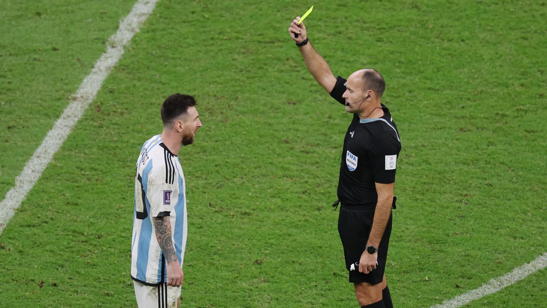 Referee Antonio Mateu shows a yellow card to Lionel Messi of Argentina.