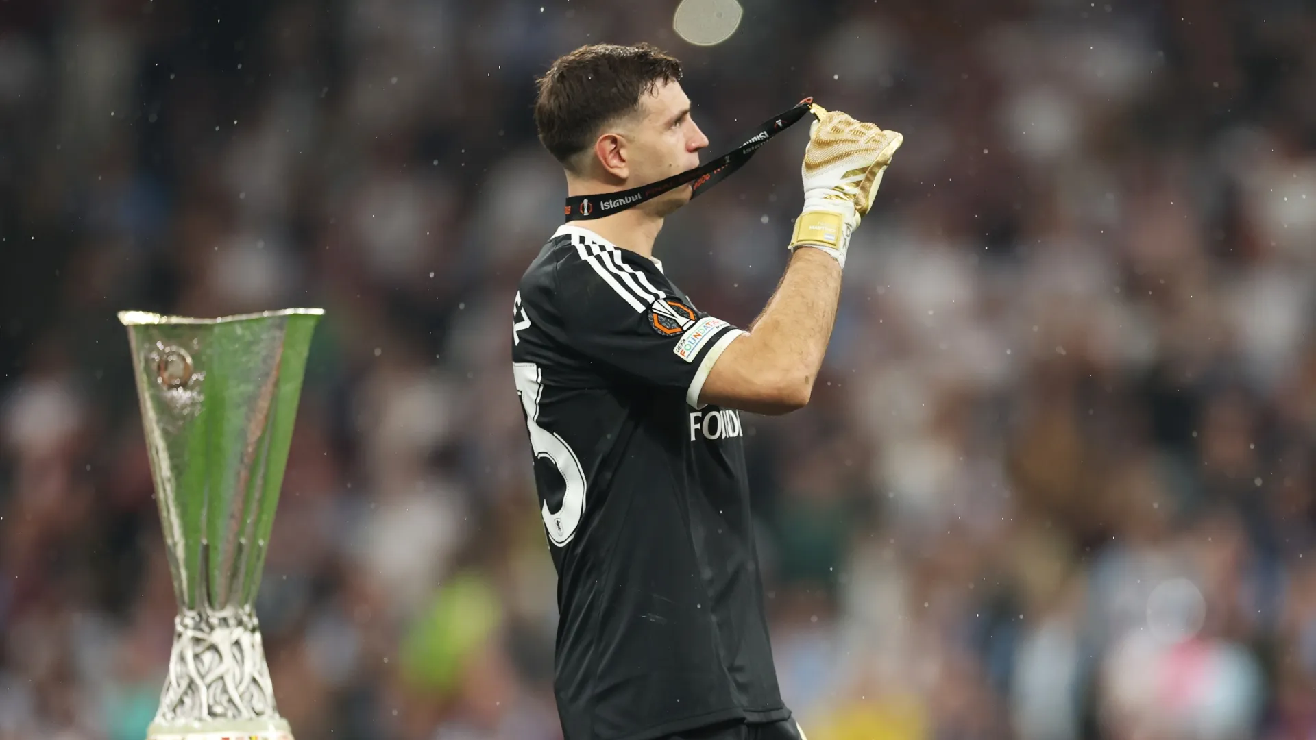 Emiliano Martinez of Aston Villa celebrates with his winners medal as he walks past the UEFA Europa League trophy.