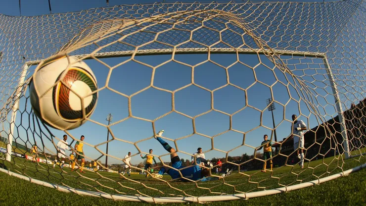 A goalkeeper is beaten by a shot