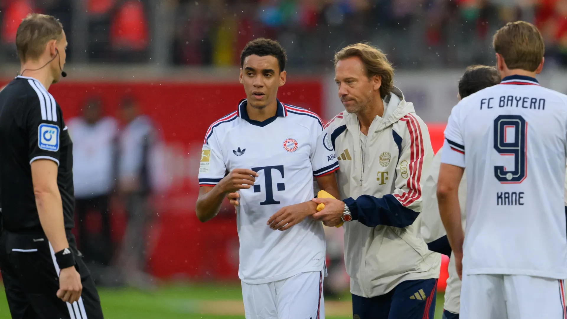 Jamal Musiala of FC Bayern Munich leaves the pitch after receiving medical treatment.